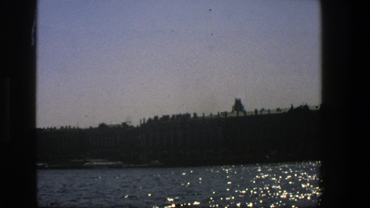 1975 Denmark 8mm view from a boat window toward sunlit water and a dark distant shoreline.