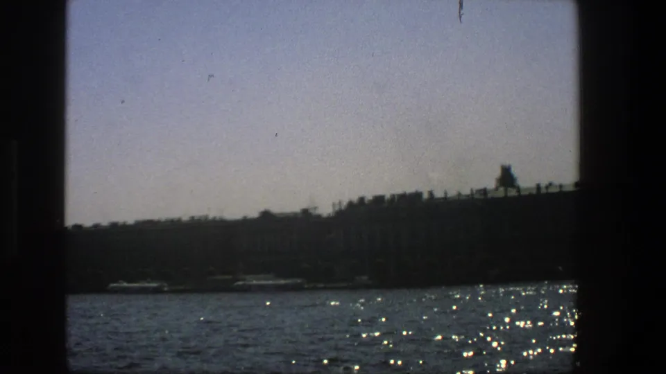 Distant Danish shoreline seen across sparkling water from a moving boat in 1975 home-movie footage.