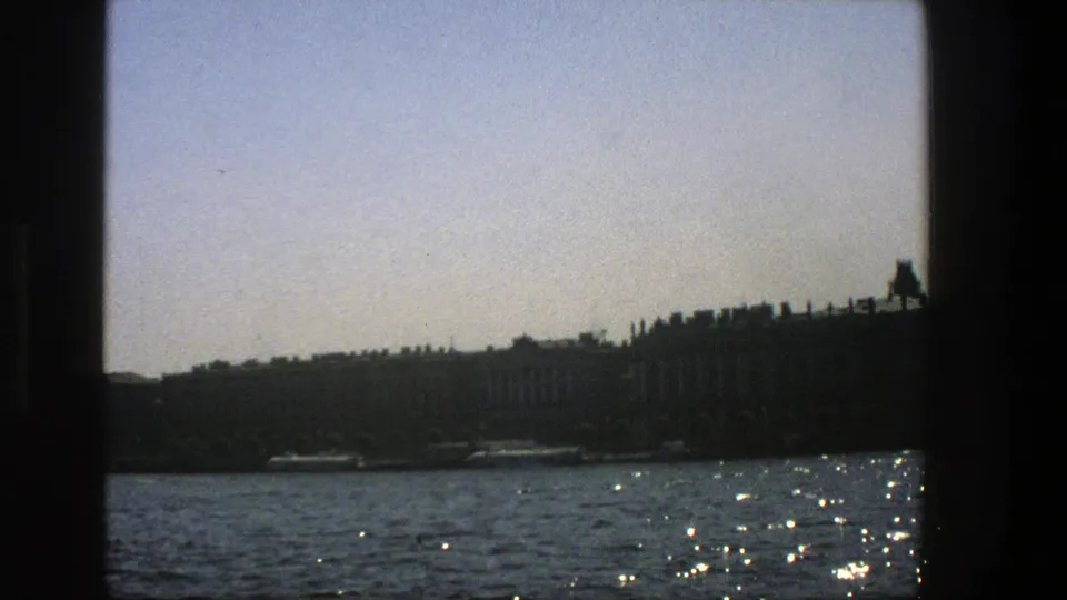 8mm boat-passenger view in Denmark, with water reflections and low shoreline buildings in silhouette.
