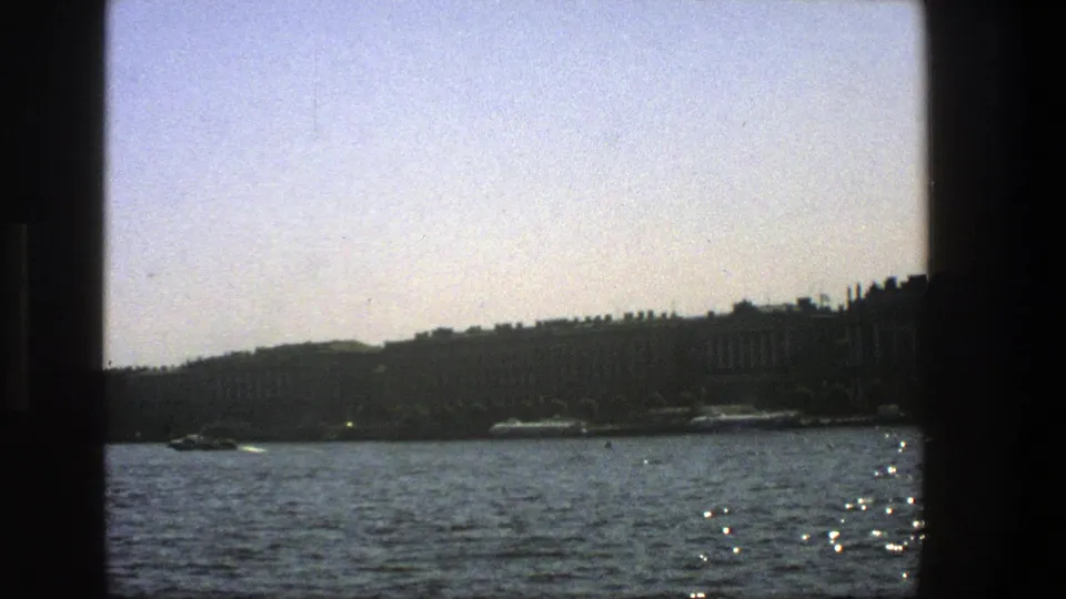 A 1975 Denmark water view shows a small craft near a distant shoreline, with dark vertical window framing at the left.