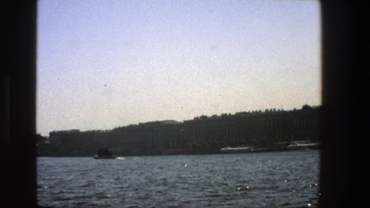 1970s 8mm boat view with blue water, a hazy distant shoreline and dark window framing around the scene.