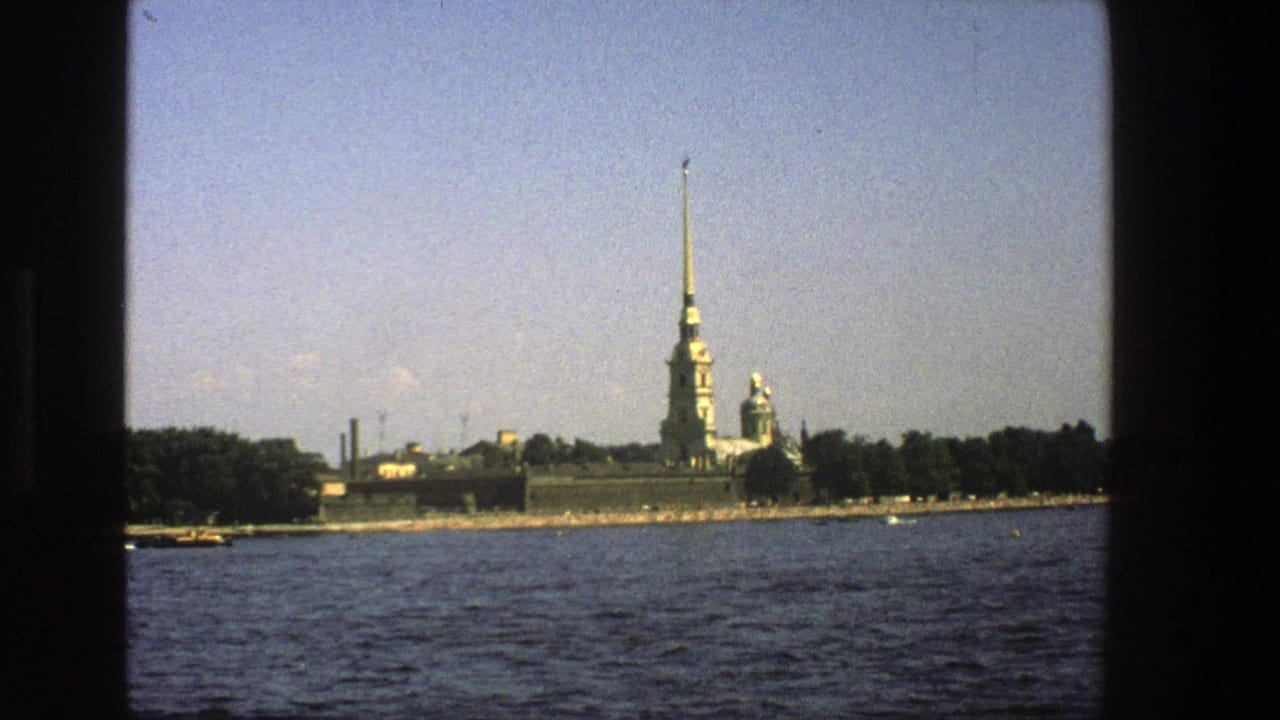 1970s 8mm travel view of a distant golden spire and historic buildings across river water, likely in Leningrad as described by clip metadata.