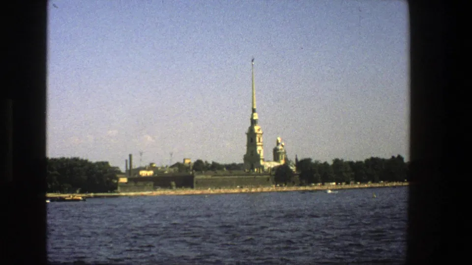 1970s 8mm travel view of a distant golden spire and historic buildings across river water, likely in Leningrad as described by clip metadata.
