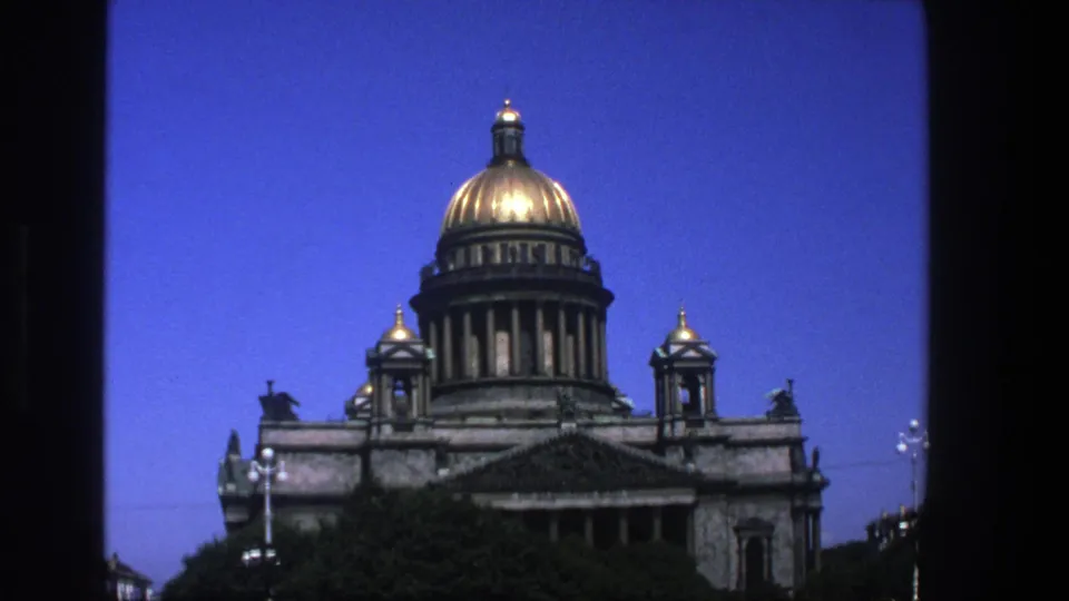 1970s 8mm view of Saint Isaac's Cathedral, with its gilded dome and stone facade framed against a deep blue sky.
