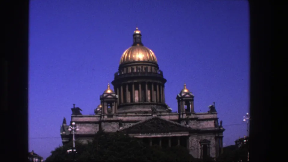 1970s 8mm view of Saint Isaac's Cathedral, showing the central gilded dome, flanking cupolas, stonework, trees, and street lamps.