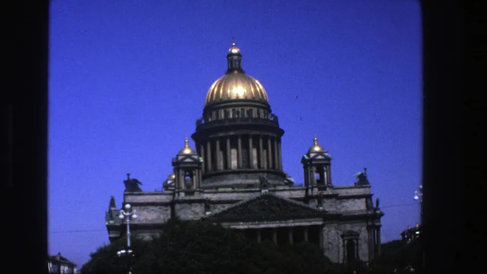 1975 8mm travel frame of a grand gold-domed building with smaller domes and a blue sky, seen through dark framing edges.