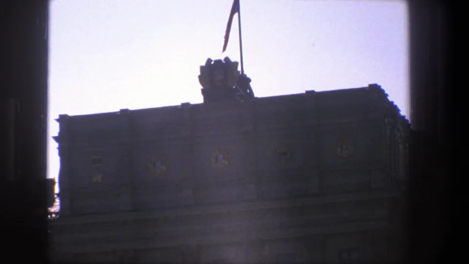 1975 Denmark home-movie frame from shade toward a bright sky, with a flag and roof ornament above a dark building facade.