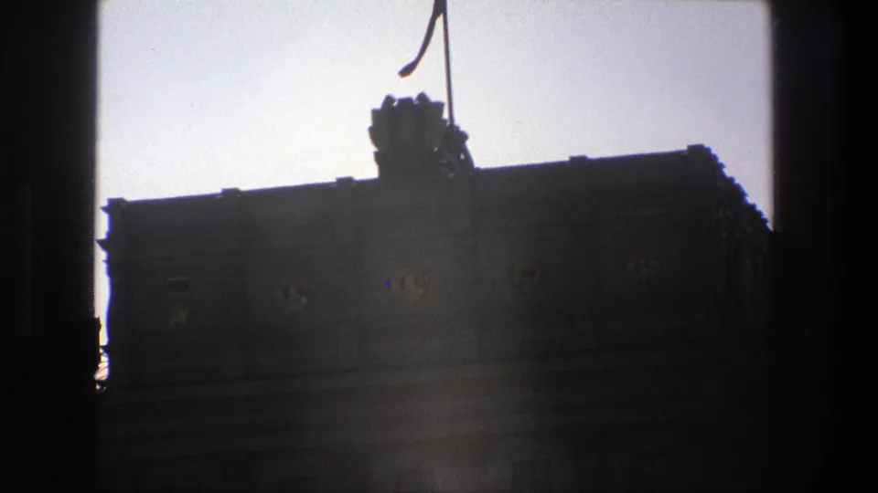1975 Denmark home-movie frame with a shadowed historic facade, rooftop ornament, and flag partially framed by dark vertical edges.