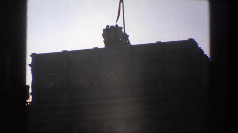 1975 Denmark 8mm frame of a dark civic facade with a roofline flag and circular emblems, partially obscured by window or gate-like borders.