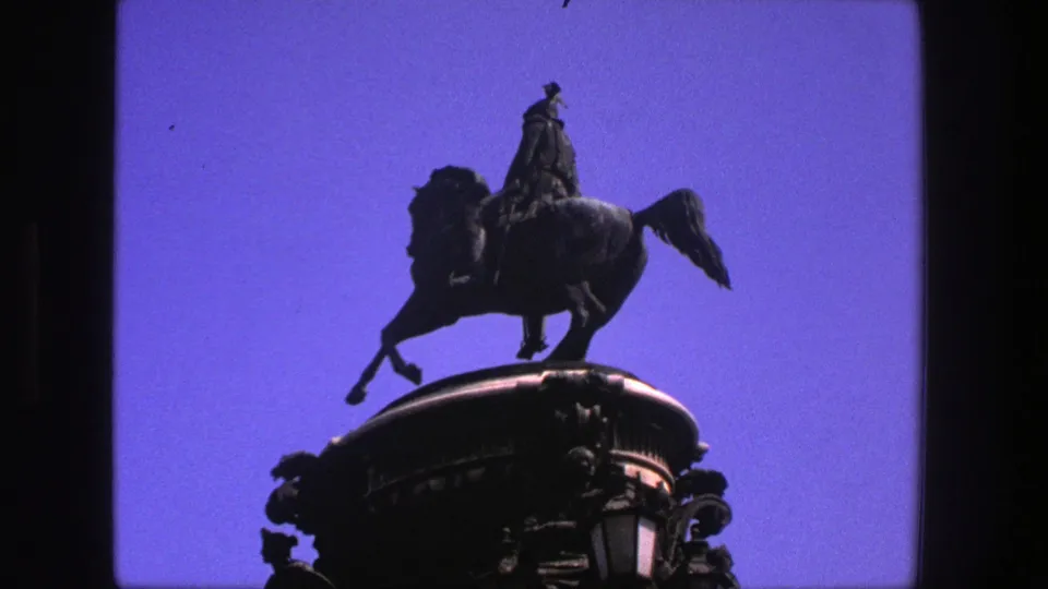 1975 Denmark 8mm frame showing a silhouetted rider on horseback atop an ornate pedestal against saturated blue sky.