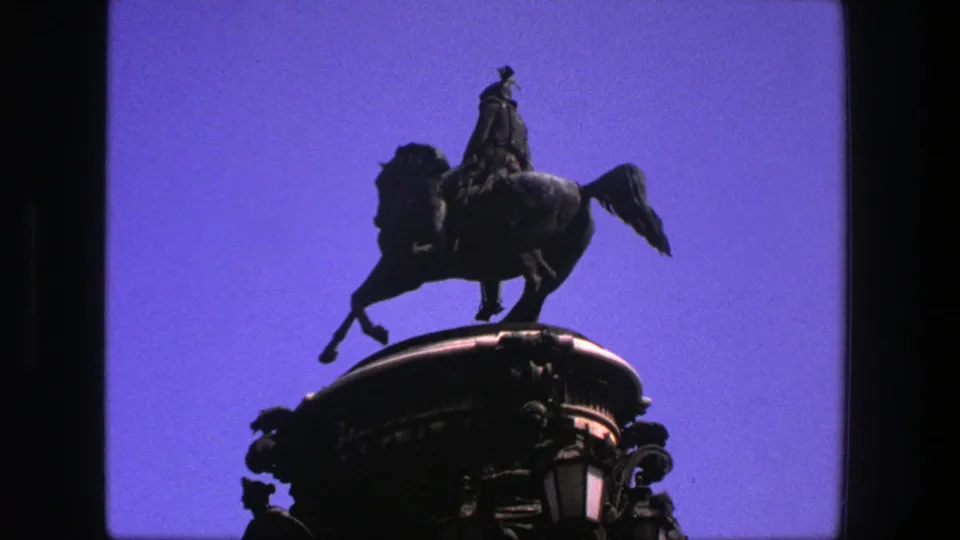 1975 Denmark 8mm frame of an equestrian statue on a rounded ornate pedestal, silhouetted against a bright blue sky.