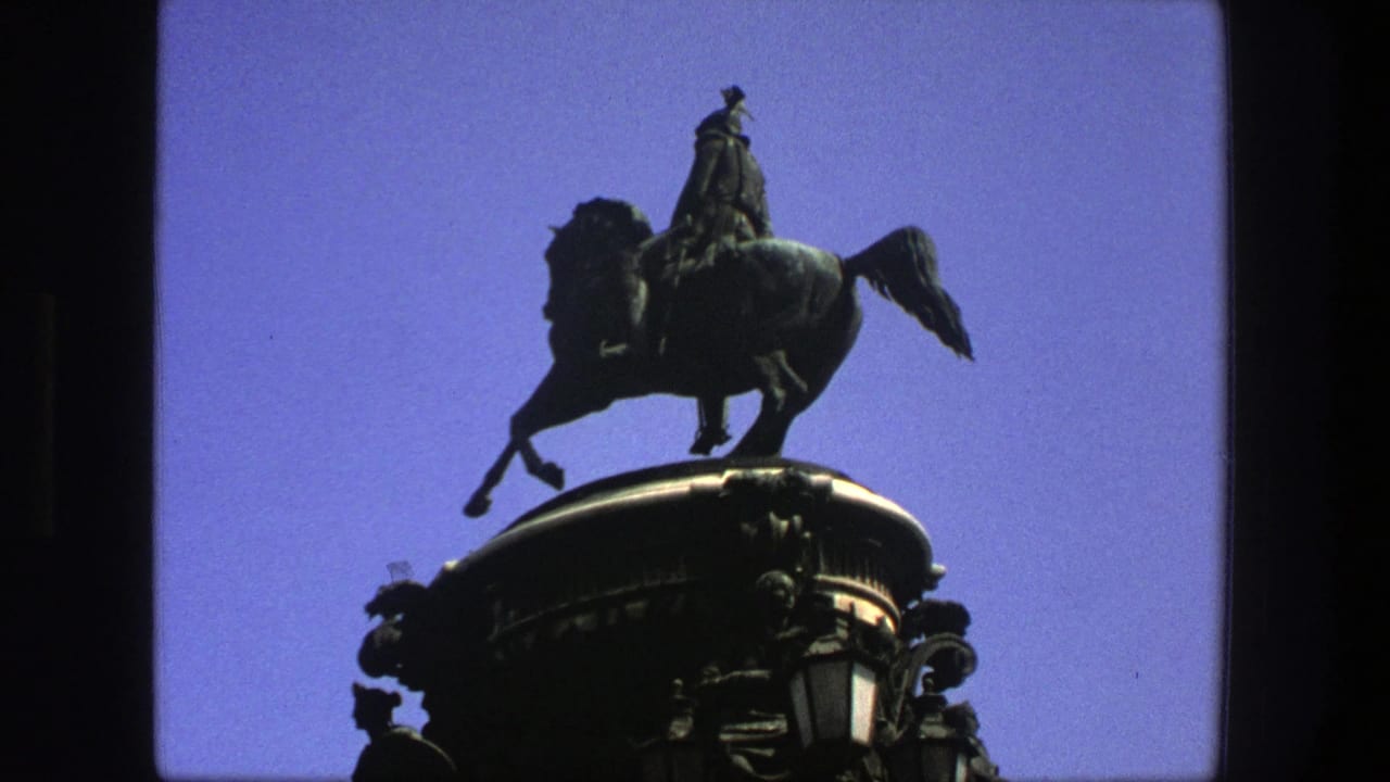 1975 Denmark 8mm frame showing a mounted rider statue silhouetted above a decorated pedestal against clear blue sky.