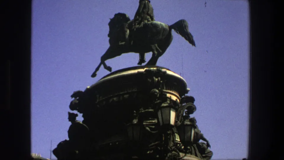 1975 Denmark 8mm frame showing the equestrian monument from close below, with sculptural details on the base visible in shadow.
