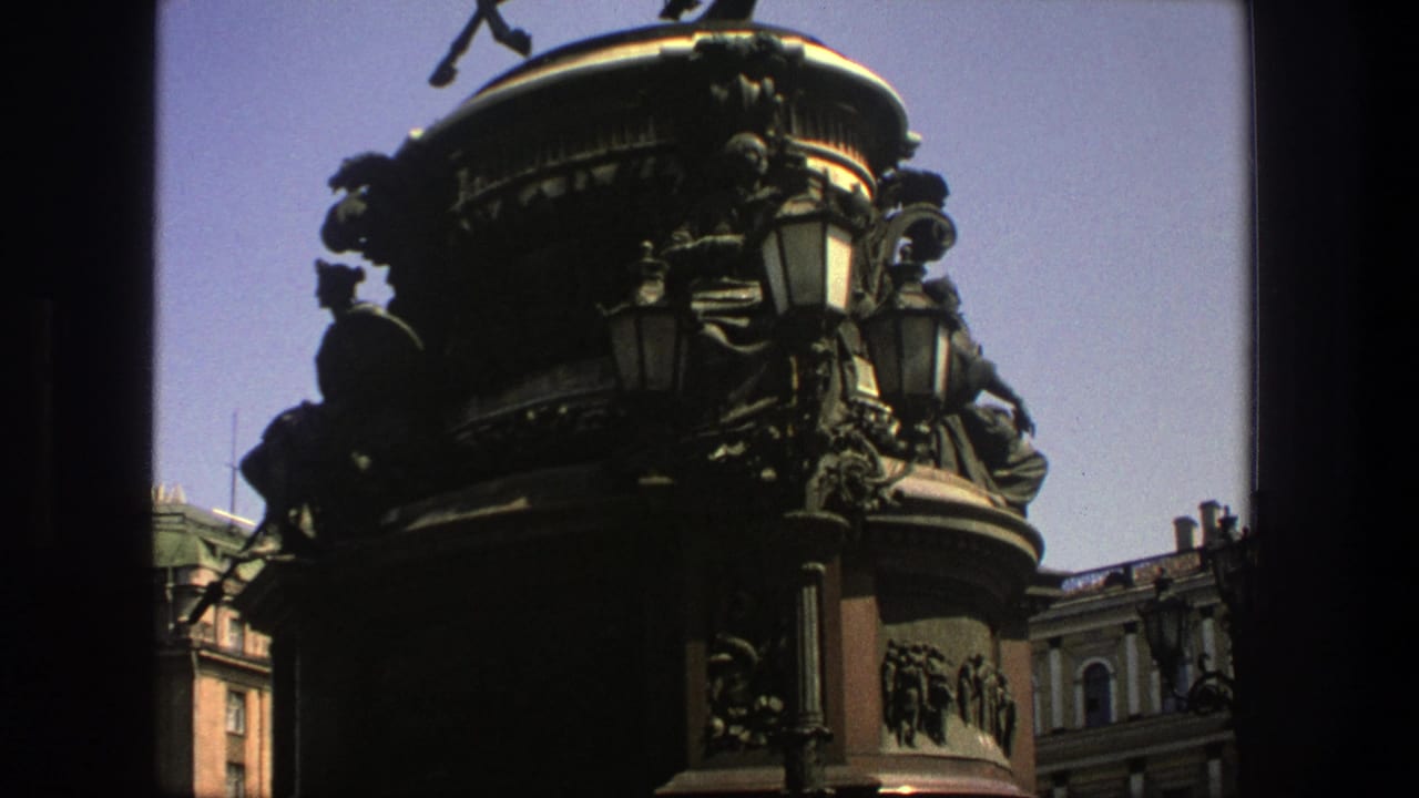 Dark monument pedestal with lamps and nearby classical buildings.