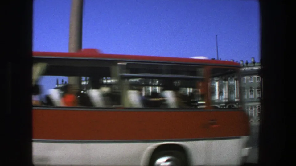 1975 Denmark 8mm frame with a red-and-white bus moving past a formal green-and-white building across a broad square.