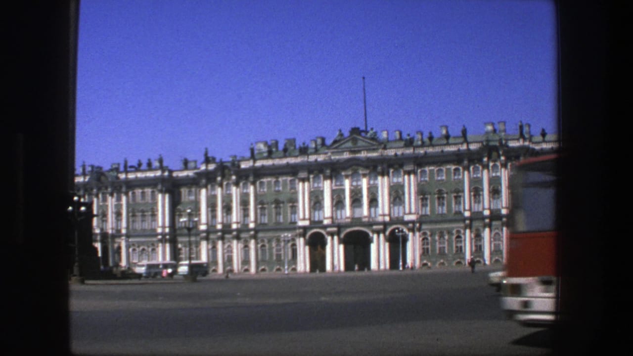 Ornate green-and-white building seen across a broad square with a bus edge at right.