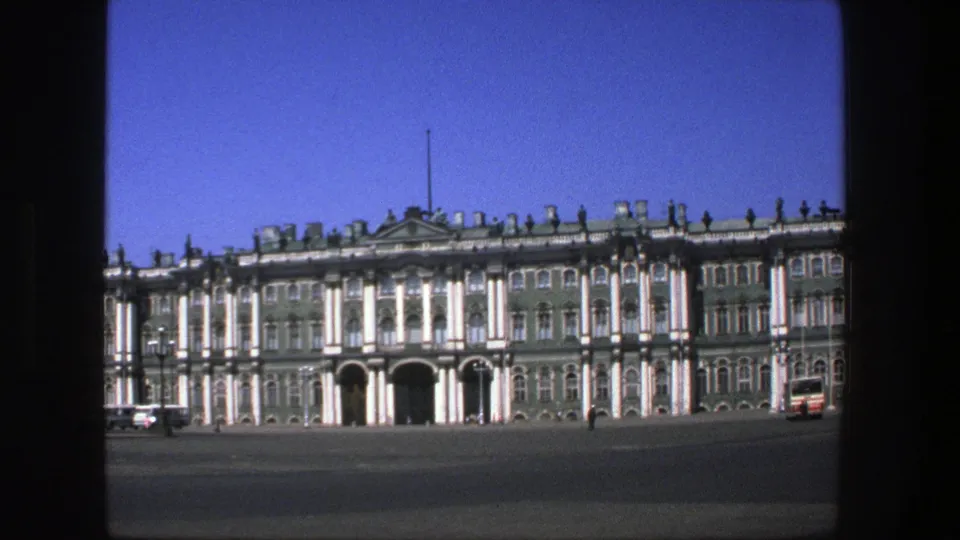 1975 Denmark 8mm frame holding on the formal building facade across the square, with distant pedestrians and a red vehicle near the right edge.