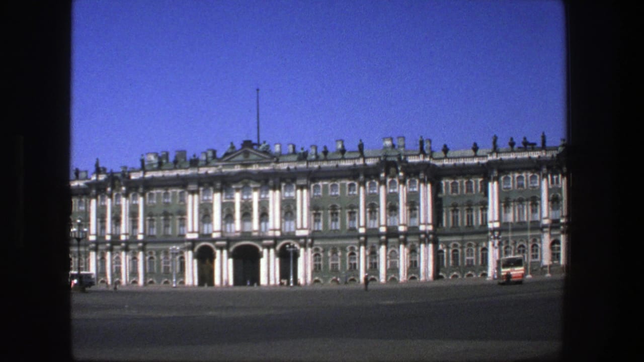 Grand green-and-white palace facade across a wide plaza under blue sky.