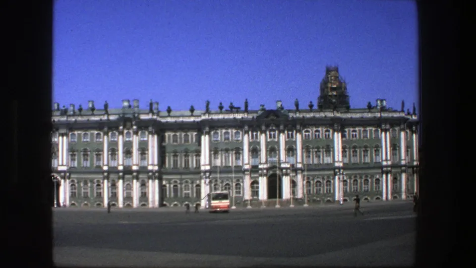 1975 8mm travel frame of a grand palace exterior in Denmark metadata, with a bus crossing the open plaza.