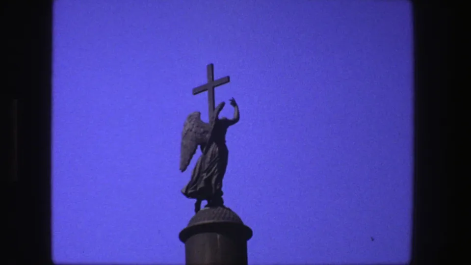 1975 Denmark 8mm frame showing a silhouetted angel statue holding a cross against a saturated blue sky.