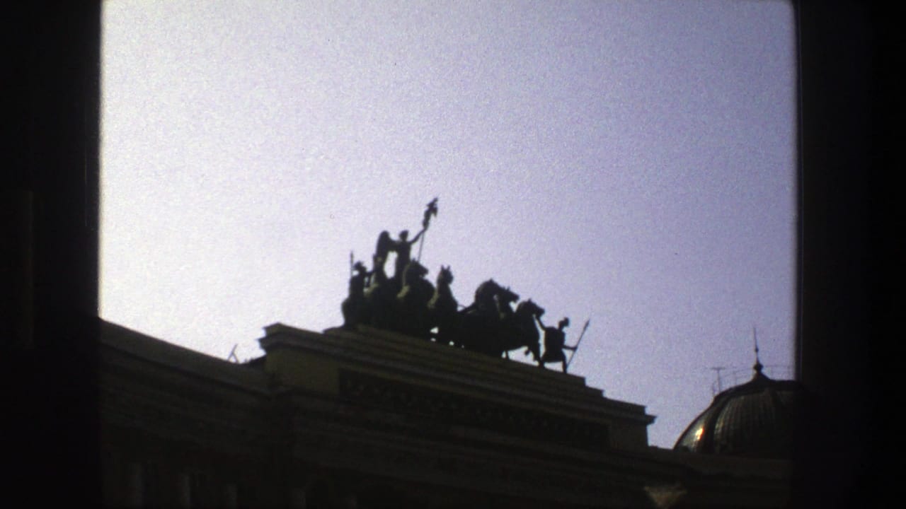 1975 Denmark 8mm frame showing a dark rooftop chariot group with horses above a classical building and pale sky.