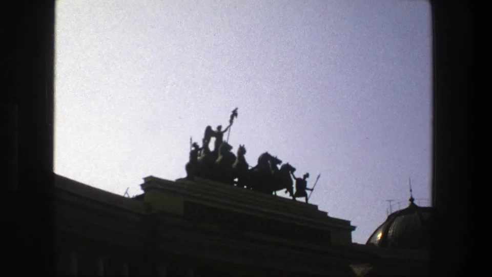1975 Denmark 8mm frame showing a dark rooftop chariot group with horses above a classical building and pale sky.