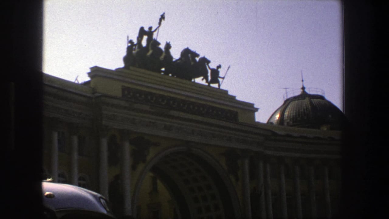 Arched building entrance, columns, dome, and rooftop statue group viewed from behind a window frame.