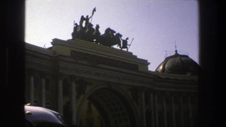 1975 Denmark home-movie frame with a classical arched facade, rooftop statuary, a domed section, and a car roof in the foreground.
