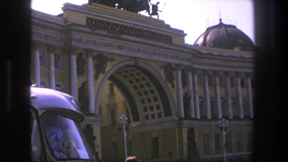 1975 Denmark bus-view frame showing a grand arched facade with columns, rooftop sculpture, and a vehicle edge in the foreground.