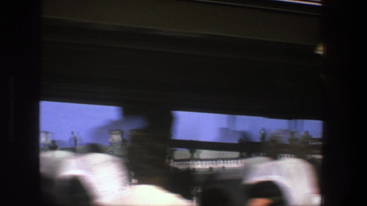 1975 Denmark 8mm frame from a moving tram, showing blurred people inside or nearby and an ornate roofline beyond the window.