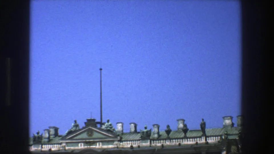 A 1975 Denmark 8mm frame shows an ornate historic roofline, statues, balustrade, and central flagpole beneath a clear blue sky.