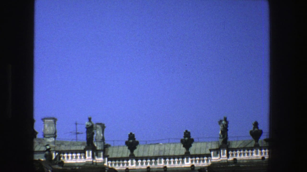 Green rooftop statues and urns above a balustrade against a clear blue sky.