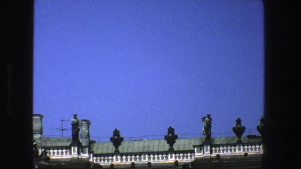 1975 Denmark travel footage frames green rooftop statuary and classical architectural details against a clear blue sky.