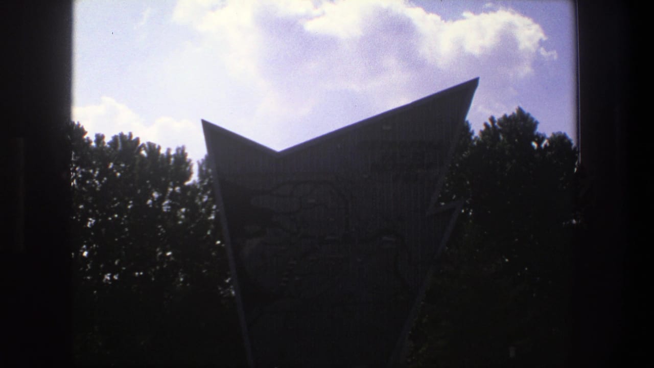 Tall angular landmark silhouetted against bright clouds with trees below.