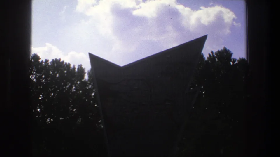 The Denmark landmark remains backlit, with its sharp roofline visible above trees and bright clouds on 8mm film.