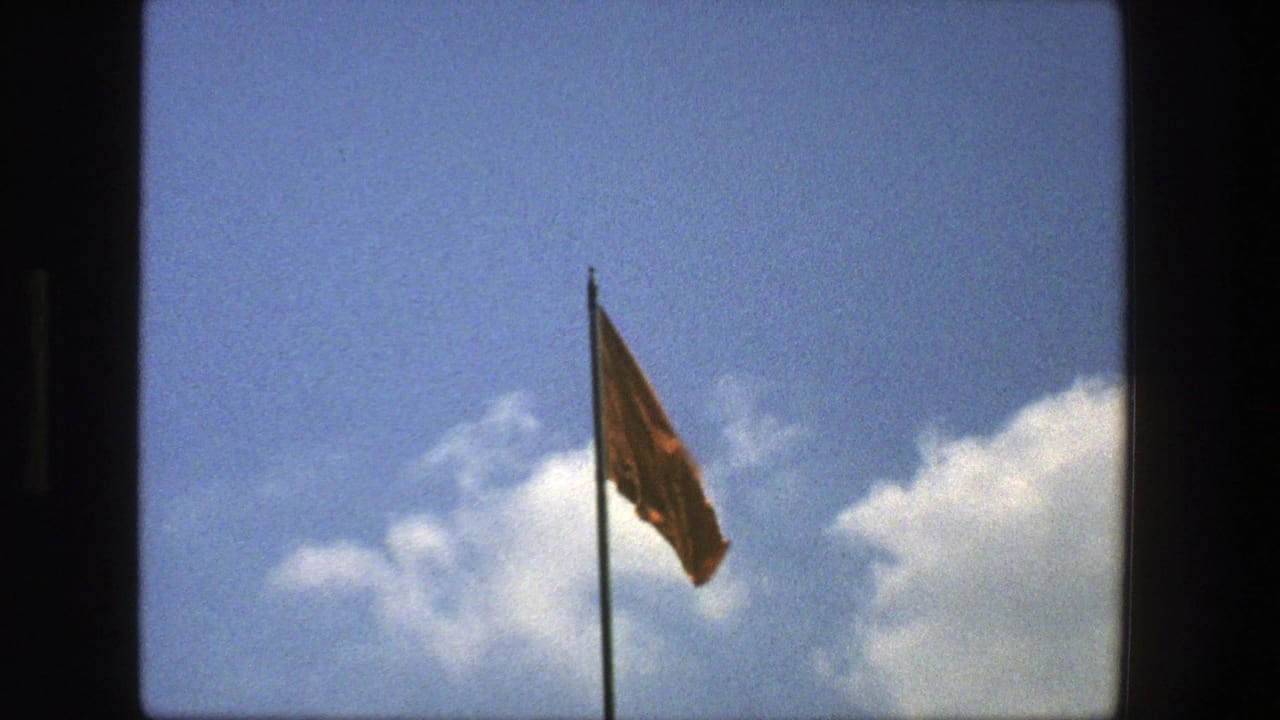 Red flag on a tall pole against blue sky and clouds.