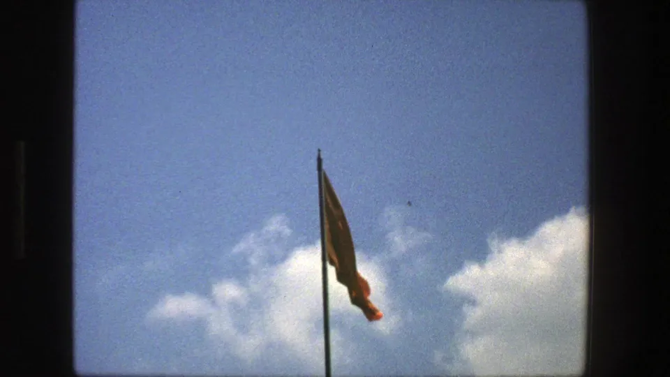 1975 Denmark 8mm frame showing a flag moving on a vertical pole, framed low against blue sky and white clouds.