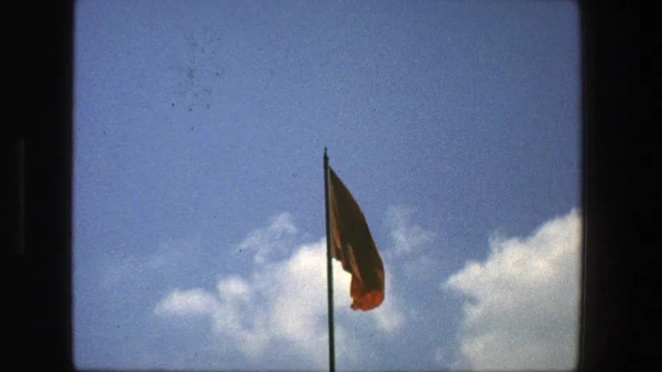 1975 Denmark 8mm frame with a red flag on a pole silhouetted against open blue sky and scattered white clouds.