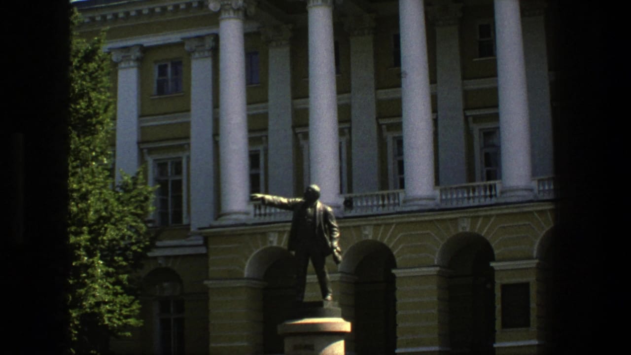Bronze pointing statue in front of a columned building with arched entrances.