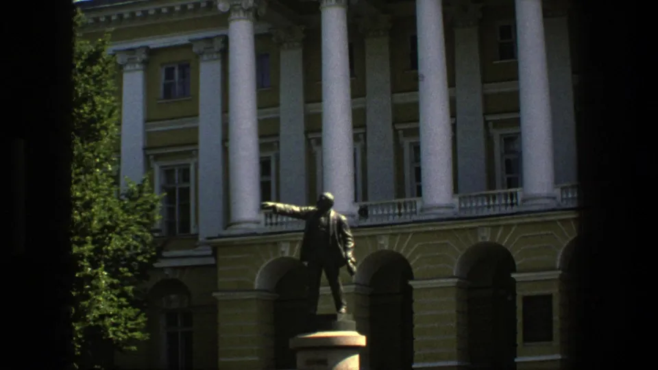 1975 Denmark 8mm frame showing a bronze pointing figure before tall white columns, arched entries, and a pale civic facade.