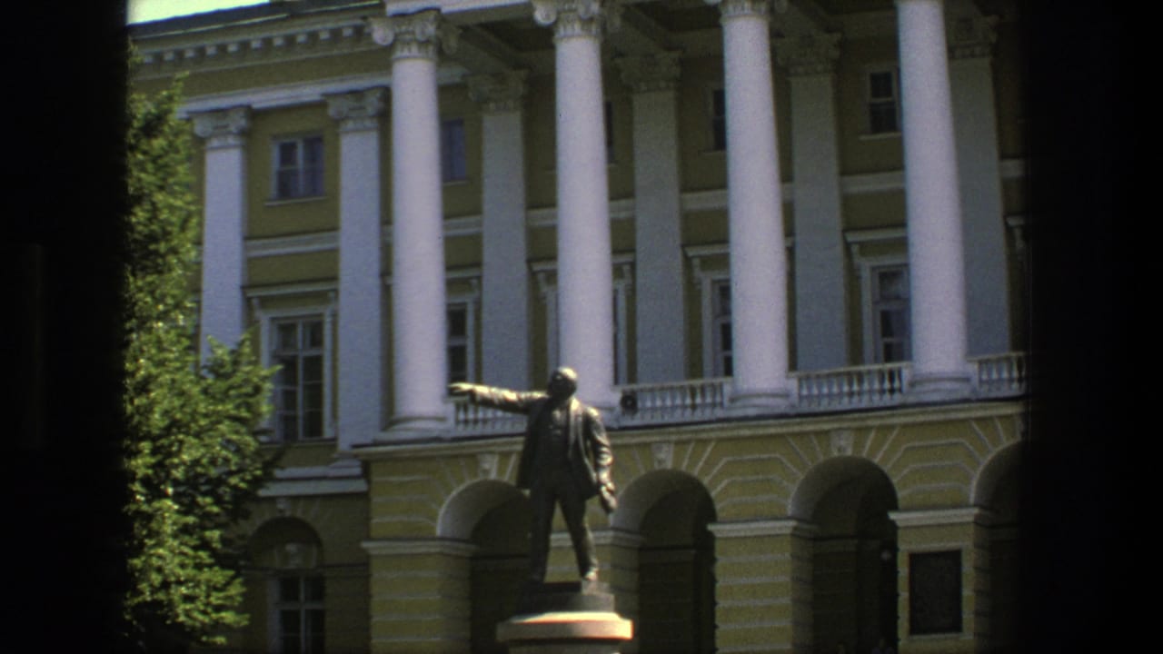 1975 Denmark frame with a bronze public statue set against a neoclassical-style facade, white columns, and shaded arches.