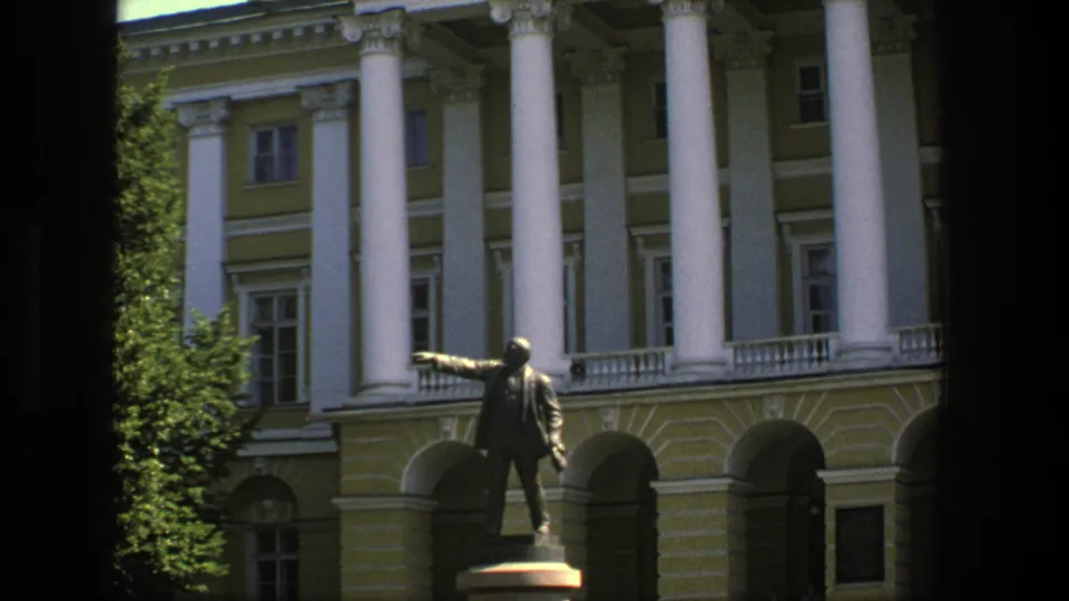 1975 Denmark frame with a bronze public statue set against a neoclassical-style facade, white columns, and shaded arches.