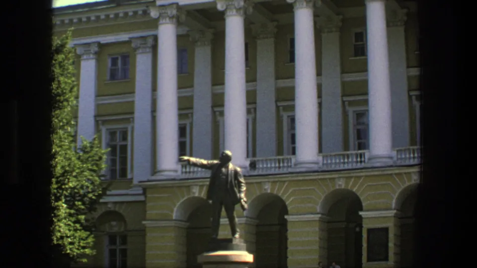 1975 Denmark 8mm frame showing the pointing bronze figure, columned facade, arched ground-floor openings, and tree shade.