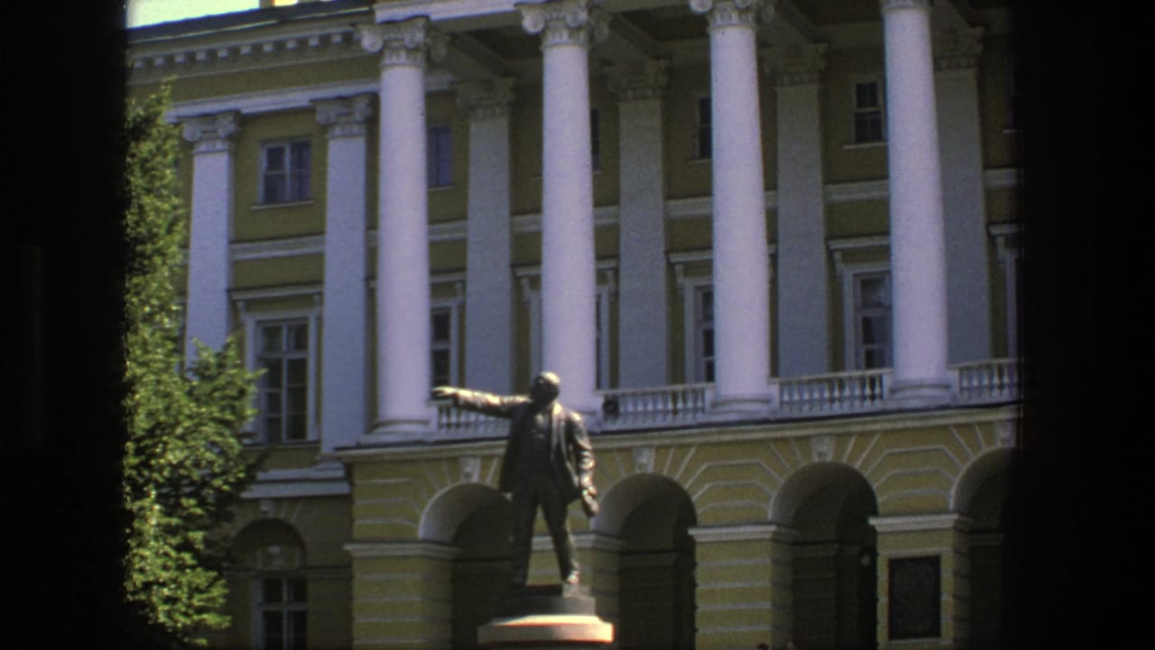 Columned yellow building with arched entries and a statue of a pointing man.