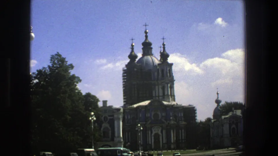 1975 8mm travel frame in Denmark showing an ornate domed church with crosses, trees, blue sky, and cars near the street.