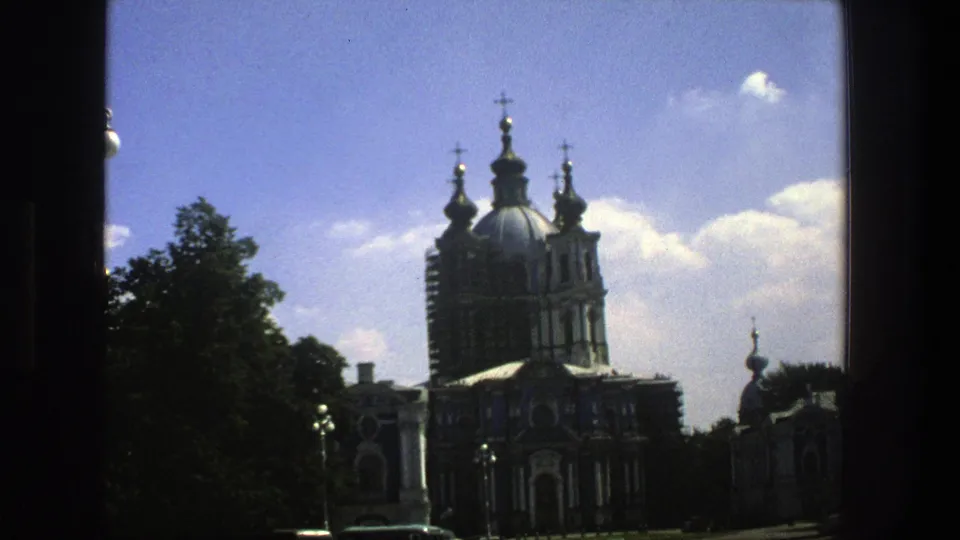 1975 8mm travel frame in Denmark showing a domed church exterior, crosses, leafy trees, bright sky, and a dark edge from the film frame.