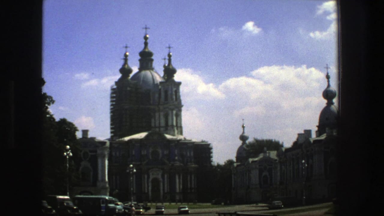 Domed Orthodox church seen from a distance with trees, cars, clouds, and dark film borders.