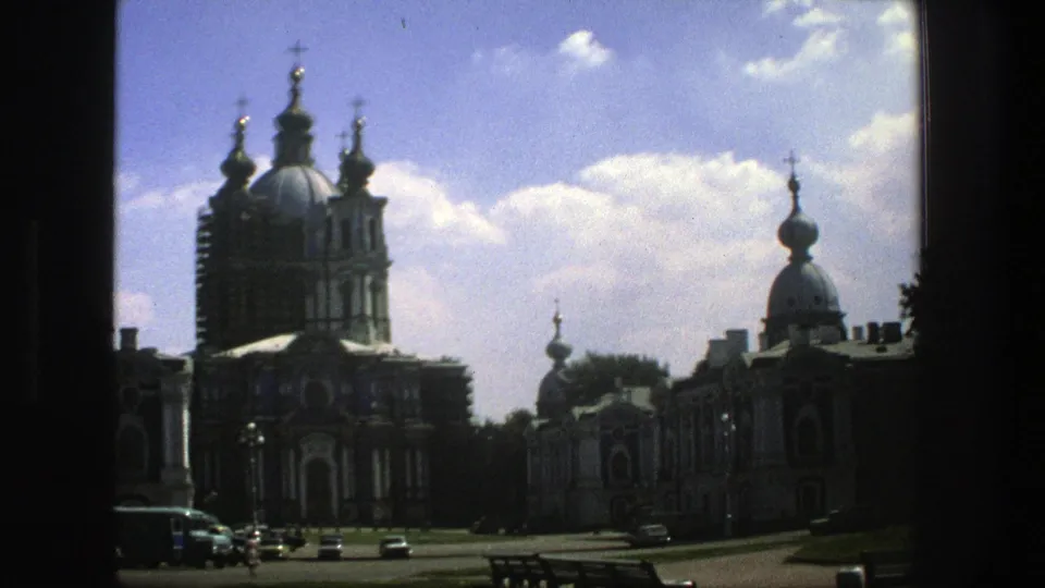 The 8mm frame brings the blue-domed Orthodox church and adjacent structure closer, with cars, a bench, trees, and open sky visible.