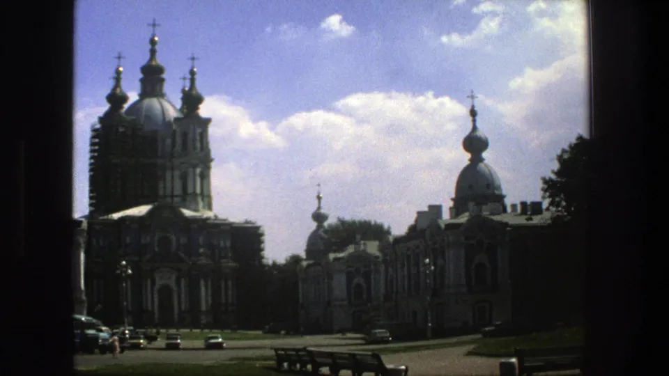 A late frame in the 1975 Denmark clip shows the domed church complex from across the road, with cars, a bench, trees, and clouds.