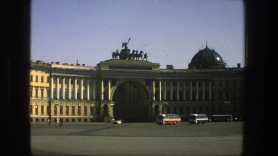 Final 1975 8mm frame in Denmark showing a quiet plaza, parked buses and cars, and a classical building with a prominent arch.